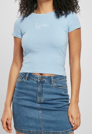 Hellblaues Crop-Top aus weichem Stoff mit kurzen Ärmeln, das ein dezentes weißes Logo auf der Brust trägt. Kombiniert mit einem Jeans-Minirock.