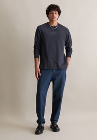 Czarna, długosleeveowa koszula w ciemnoszarym kolorze z okrągłym dekoltem i subtelnym logotypem na piersi, zestawiona z ciemnoniebieskimi spodniami typu wide-leg i czarnymi butami.