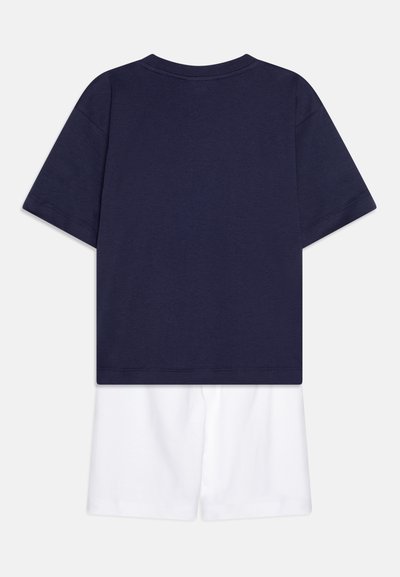 Camiseta de algodón azul marino de manga corta y cuello redondo; combinada con pantalones cortos de algodón blancos. Diseño simple, sin patrones ni acentos.