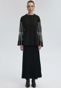 Black knit top with white vertical stripes on sleeves, paired with a long black pleated skirt and black ankle boots. Simple, modern design.