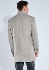 Hellgrauer Fischgrätenmantel mit hohem Kragen, langen Ärmeln und geknöpften Manschetten, mit geradem Schnitt und strukturierter Stoffqualität.