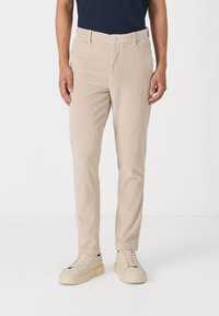 Beige corduroy bukser med lige pasform, der har lodret ribbing, knaplukning og sidelommer. Båret med lysfarvede sneakers.