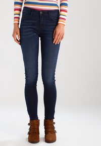Mörkblå skinny jeans i denim med en slät yta, tillsammans med bruna ankelboots med flera spännen.