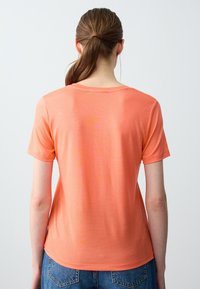 Maglietta a maniche corte, morbida e leggera, di colore corallo; scollo rotondo, texture liscia, con dettagli di cucitura sottili e una vestibilità rilassata.