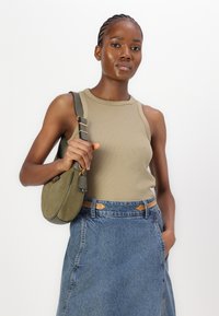 Oliven grønn ribbestrikket tanktop kombinert med en denimskjørt og en sirkulær oliven grønn skulderveske med gull detaljer.