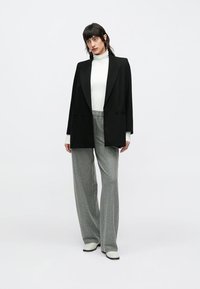 Sort skræddersyet blazer med spidse revers, hvid højhalset trøje og grå bukser med brede ben og lodrette striber; med glat front og subtile detaljer.