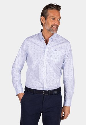Lichtblauwe blouse met lange mouwen en donkere stippen, met een button-down kraag en een linkse borstzak, gecombineerd met donkerblauwe broeken en een gevlochten riem.