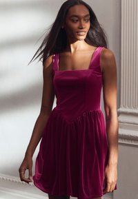 Fuchsia Samtkleid mit quadratischem Ausschnitt, breiten Trägern, tailliertem Oberteil und einem lockeren, gerafften Rock. Weicher Stoff mit dezentem Glanz.