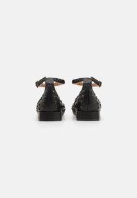 Crne kožne cipele s podesivim anklets trakom, s okruglim metalnim zakovicama sa strane i ravnim potplatom. Glatka tekstura, minimalistički dizajn.