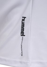 Weißer Stoff mit schwarzem "hummel PERFORMANCE"-Text, der vertikal nahe einer Naht auf einem Sportbekleidungsstück gedruckt ist.