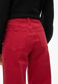 Punane denim püksid sirge lõikega, millel on kaks tagumist taskut, tikitud detailid ja sile tekstuur.
