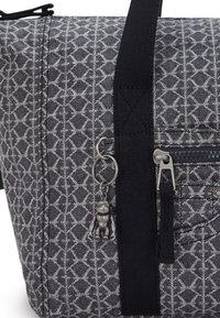 Grå mönstrad väska med textilmaterial, har en svart rem, en dragkedjeficka och en dekorativ charm fäst.