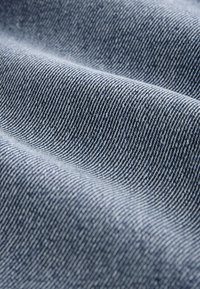 Denimkangas, millel on sile tekstuur ja sinise-valgete triipudega muster, kuvades sügavust ja kergeid variatsioone koemustris.