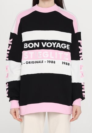 Personne portant un sweat-shirt rayé noir, blanc et rose avec le texte « BON VOYAGE STIEGLITZ ORIGINALE 1988 » sur le devant et les manches.