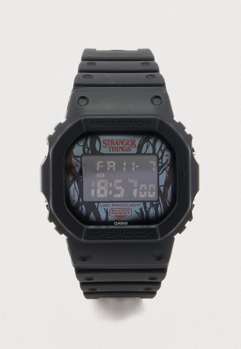 Ceas G-Shock negru cu afișaj digital dreptunghiular, având design „Stranger Things” pe fundal, curea texturată din cauciuc și iluminare LED de fundal.