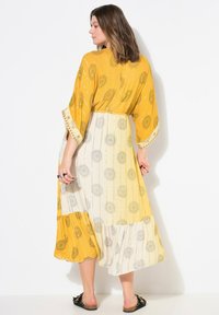 Abito giallo e crema con motivo, maniche corte, orlo a contrasto e dettagli metallici. Tessuto fluido con motivi floreali.