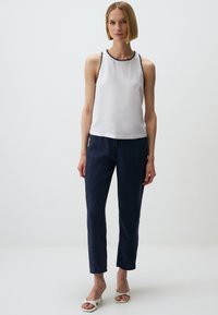 Witte mouwloze top met zwarte bies, gecombineerd met marineblauwe tapered broek en witte open teen hakken, die een simpele en strakke uitstraling tonen.