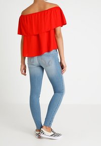 Röd off-shoulder topp med volanger, parat med ljusblå skinny jeans och rutiga slip-on skor.