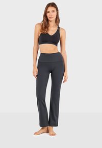 Soutien-gorge de sport noir avec garniture blanche et leggings gris taille haute, tous deux en tissu lisse et extensible. Présente un design à jambes évasées.