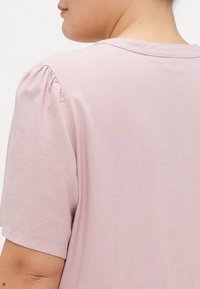 Ροζ κοντομάνικο πουκάμισο με στρογγυλή λαιμόκοψη και ραμμένα μανίκια, φτιαγμένο από μαλακό ύφασμα με λεία υφή.