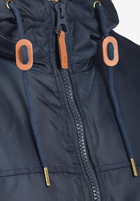 Primo piano della cerniera di una giacca blu navy con tirante in pelle e cordini blu infilati in occhielli marroni con punte in ottone.