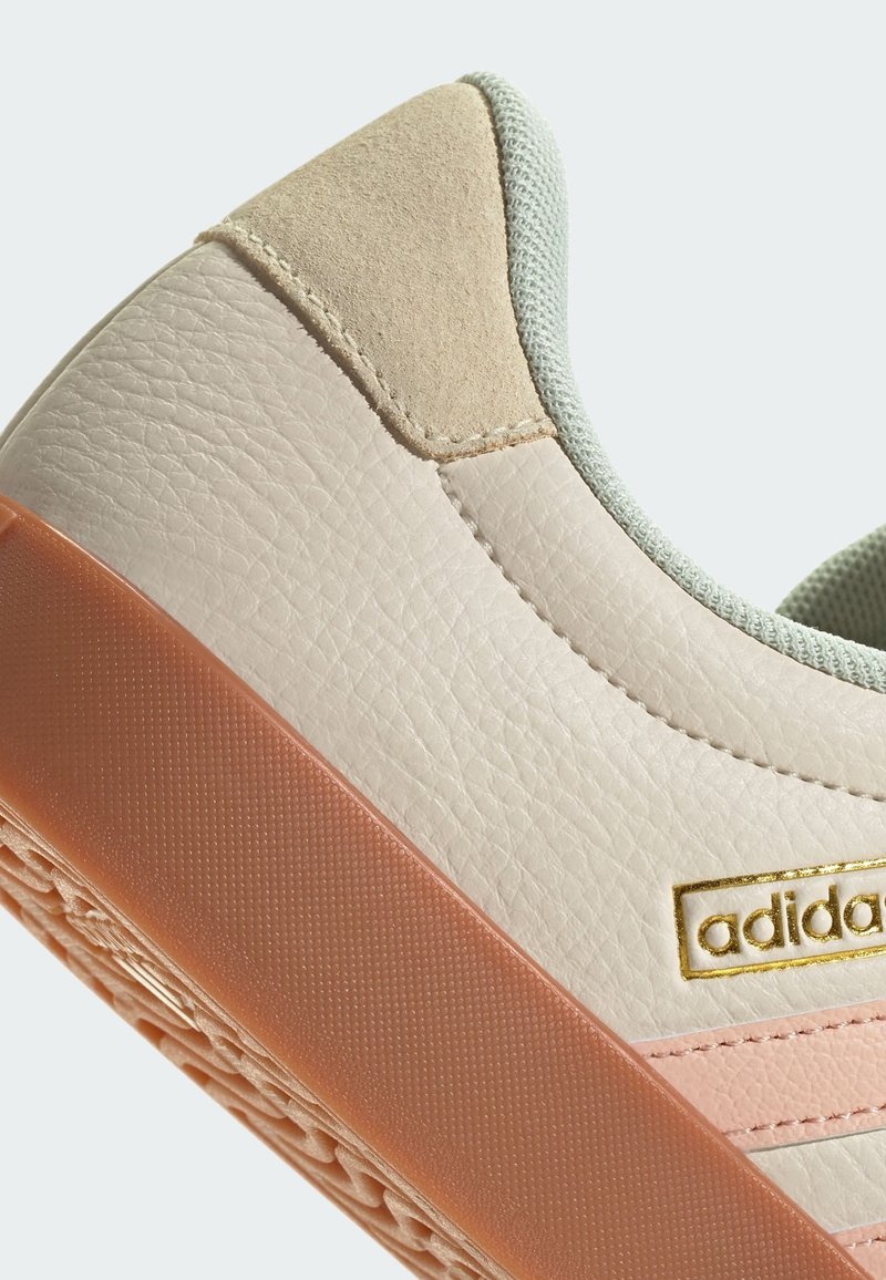 Baskets en cuir beige avec un talon en daim doux, des rayures roses et une semelle en caoutchouc orange texturé. Accent logo en or sur le côté.
