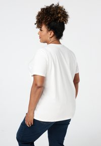 T-shirt blanc à manches courtes avec un col rond et une coupe décontractée. Le tissu semble doux, avec une texture lisse.