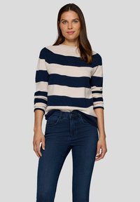 Gestreifter Pullover mit horizontalen Streifen in Marineblau und Beige. Strickmaterial, Rundhalsausschnitt, langärmlig mit hochgeschobenen Ärmeln, kombiniert mit dunkler Jeans.