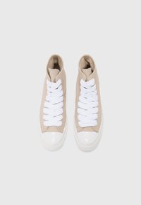 Sneakers înalte bej cu șireturi albe, din material textil, cu vârful rotunjit și un capac din cauciuc alb lucios în față.