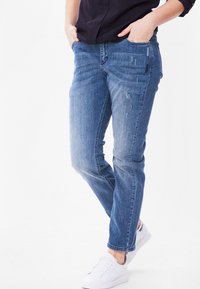 Jeans i mellanblått med en lätt sliten finish, rak bendesign, främre fickor och vita sneakers för kontrast.