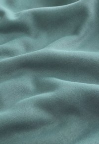 Tessuto di cotone in un delicato colore teal, che mostra una texture liscia con morbide pieghe e un sottile motivo a maglia.
