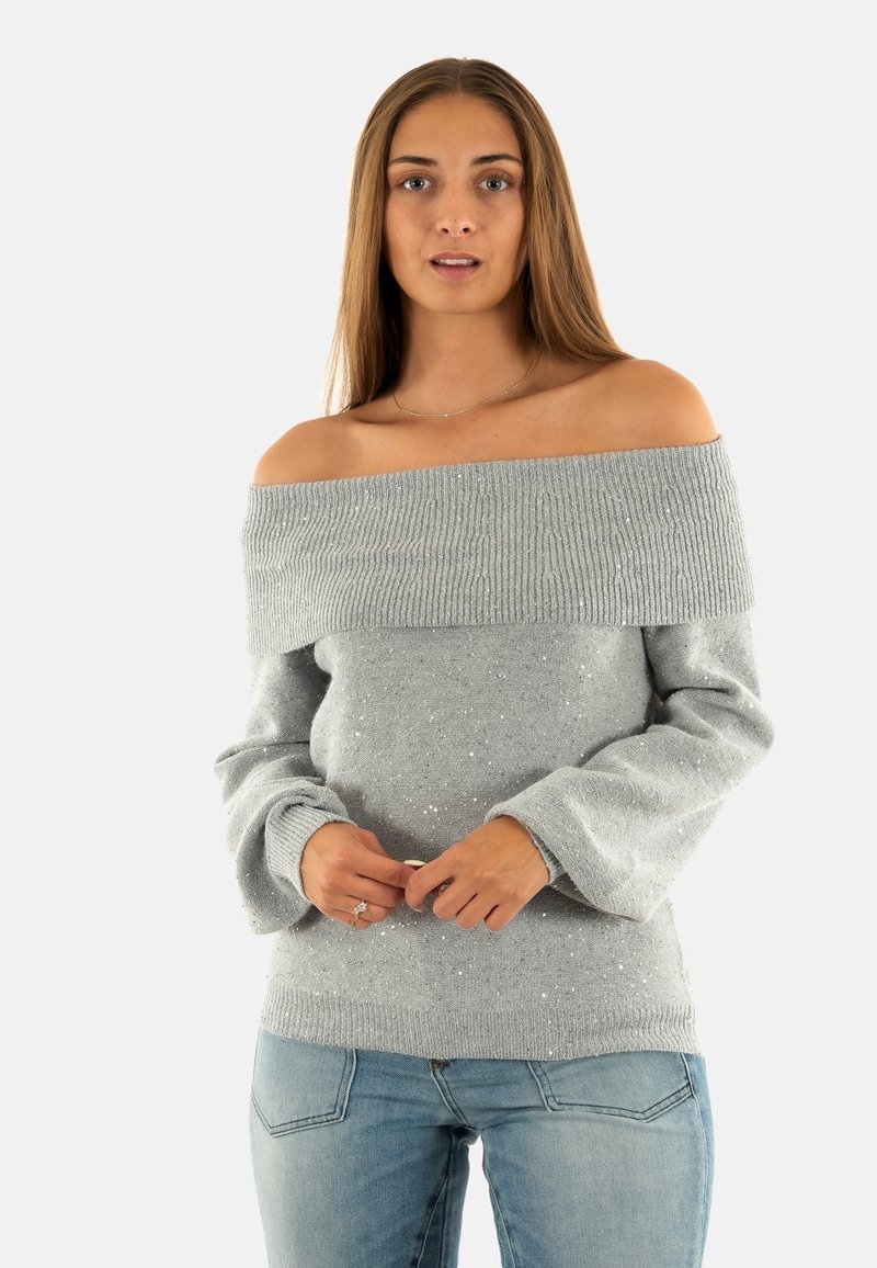 Maglione grigio off-the-shoulder con scollatura a coste, morbido al tatto e con dettagli di glitter sparsi, abbinato a jeans azzurri chiari.