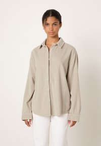 Gaiši pelēka kordurojas krekls ar apkakli un pogu priekšpusi, ar atslābinātu piegriezumu un garām piedurknēm, kombinēts ar baltām biksēm.