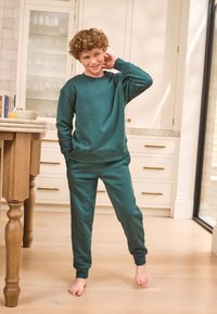 Sweat-shirt bleu sarcelle et pantalon de jogging assorti en tissu doux. La tenue présente une coupe décontractée, un col rond et des poignets côtelés.