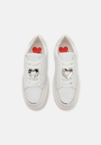 Baskets blanches avec une finition en cuir lisse, ferrure en forme de cœur sur les lacets, et impression rouge "LOVE" à l'intérieur. Bout arrondi et semelle rembourrée.