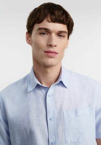 Jasnoniebieska, krótka koszula z rękawami, wykonana z lnu. Posiada zapięcie na guziki z przodu oraz kieszeń na lewej piersi. Miękka, teksturowana tkanina o luźnym kroju.