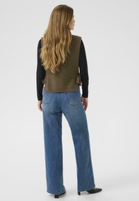Strikket olivengr�øn vest med ribbet tekstur, parret med højtaljede lyseblå jeans med lige ben og femlommer-design.