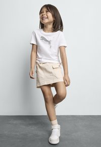 T-shirt en coton blanc avec logo Puma gris, jupe style cargo beige, baskets montantes blanches avec accents roses, et chaussettes beiges.