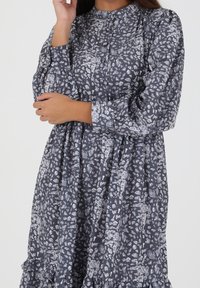 Vestido de manga larga en gris oscuro con un patrón abstracto en gris claro, con cuello alto y dobladillo con volantes. Tejido suave con un ajuste holgado.