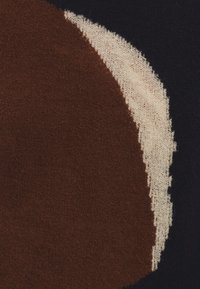 Strickstoff mit einem braunen, kreisförmigen Design, das von einem cremigen und marineblauen Hintergrund umrandet wird. Weiche Textur mit deutlichem Farbkontrast.