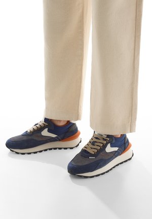 Sneakers blu navy e grigi con un logo bianco e dettagli arancioni; upper in mesh testurizzato e suede, collare imbottito e suola in gomma nera.