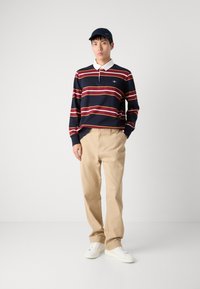 Marine-stripete langermet polo med hvit krage, kombinert med beige bukser og hvite sneakers. Kappen er mørk marineblå. Enkel, uformell design.