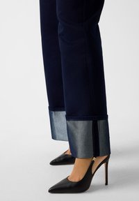 Τζιν παντελόνια σκουρομπλε με ψηλή μέση, με αντίθεση ανοιχτομπλε μανσέτα και λεπτομέρεια φερμουάρ, σε συνδυασμό με μαύρες στιλέτο γόβες.