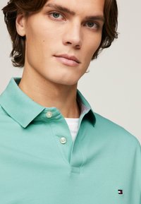Polo de color verde claro con mangas cortas, tapeta de botones y una sutil textura en la tela; presenta un pequeño logo en el pecho.