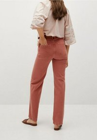 Jean rose à coupe droite, cinq poches, détails cousus, associé à un chemisier léger et texturé ainsi qu'à des sandales.