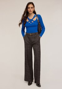 Top blu ribbed a maniche lunghe con dettagli a taglio, abbinato a pantaloni larghi a quadri grigi e stivaletti neri con tacco. Cintura e borsa marroni incluse.