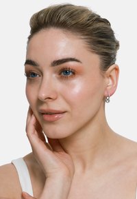Orecchini a cerchio in argento sterling con un design moderno, caratterizzati da una finitura lucida e dettagli a cerchio interconnessi. Pelle liscia e trucco naturale.