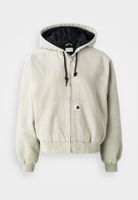 Hettegenser med glidelås i lys beige bomull; quiltert svart innside, justerbare snorer, to frontlommer og elastiske ermer.