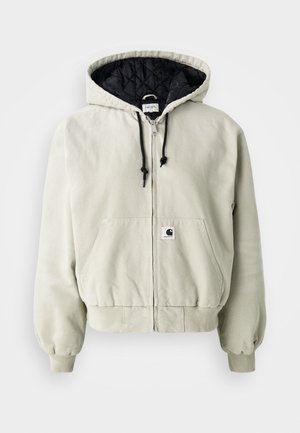 Chaqueta con capucha y cremallera en algodón beige claro; interior acolchado negro, cordones ajustables, dos bolsillos frontales y puños elásticos.