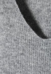 Zbliżenie miękkiej szarej dzianiny z prążkowaną fakturą oraz widocznymi delikatnymi włóknami i fałdami.